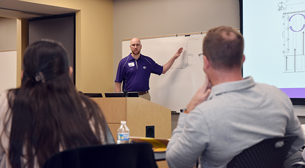 Instructor gesturing to diagram on white board while teaching class. 