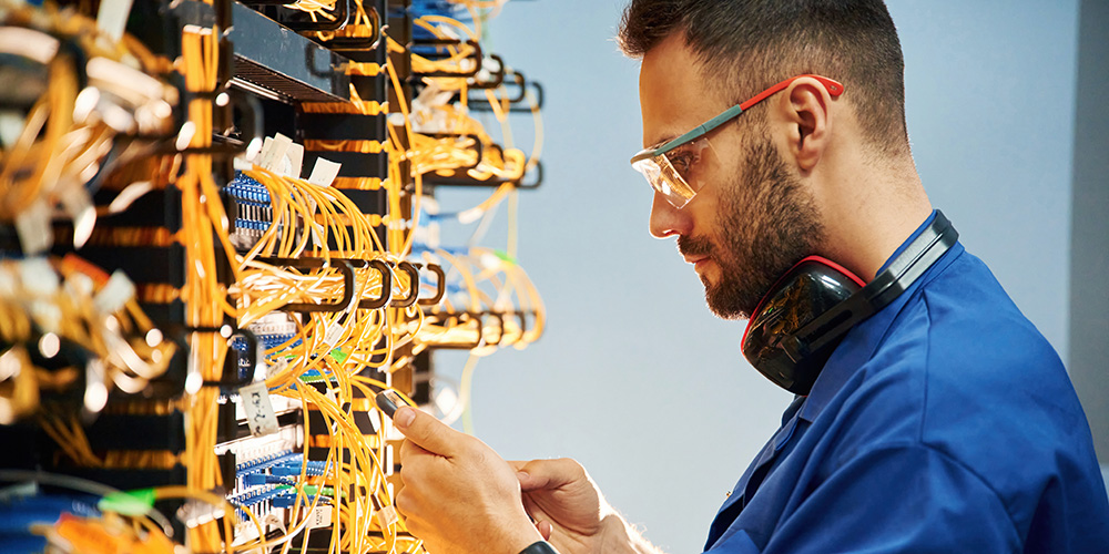 Young man connecting cables in the back ports of server boxes.