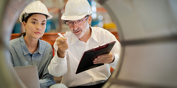 Middle-aged man showing a younger coworker an object on the production floor. 