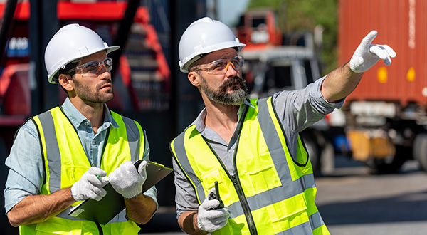 Man wearing hard hat and safety vest interacts with touchscreen monitor attached to industrial equipment.