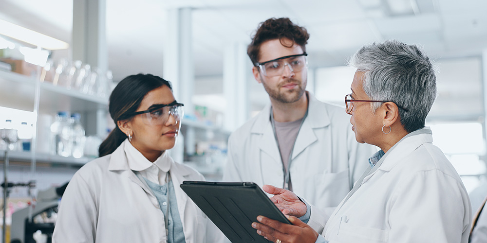 Older scientist talking to two younger scientists in a lab.