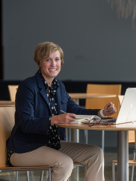 Student with laptop sitting in the Bistro at the K-State Olathe campus smiling.