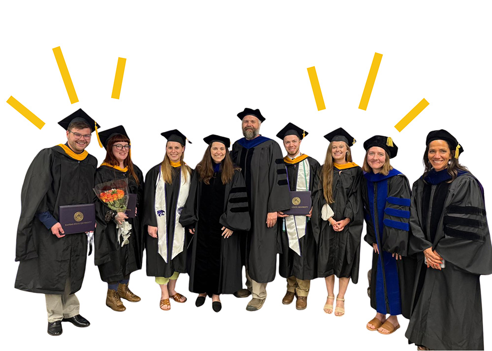 Photo of recent graduate students in their caps and gowns standing with their advisors and instructors. 